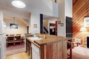 A modern kitchen with a central island, wooden ceiling, and a dining area with chairs. - Comfy, lofted condo close to slopes with balcony, views, hot tub, & fireplace (Mammoth Lakes)