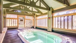 Una piscina interior con escalera, vigas de madera y ventanas grandes.
