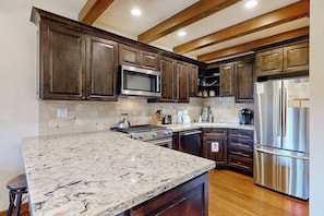 A kitchen with dark wooden cabinets, stainless steel appliances, and a marble countertop. - Sophisticated, dog-friendly condo in nature with fireplace - walk to village (Mammoth Lakes)