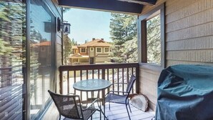 Een overdekt terras met een tafel, stoelen, een barbecue en uitzicht op een huis.