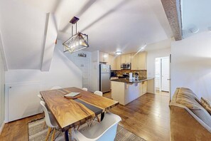 Eine moderne Küche mit einer zentralen Kochinsel, weißen Schränken und einem Essbereich mit Holztisch und weißen Stühlen.