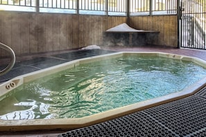 Ein Whirlpool mit einer hölzernen Sitzbank und Metallgeländer, umgeben von einem Holzzaun und einem Metallgitter.