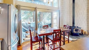 Een keuken met een groot raam, een eettafel met stoelen, een koelkast en een houtkachel.