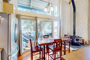 Eine Küche mit großem Fenster, einem Esstisch mit Stühlen, einem Kühlschrank und einem Holzofen.