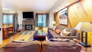A living room with a fireplace, a television, a sofa, and a dining area with a table and chairs. - Updated Ground-floor Condo with On-site Pool, Hot Tub, Sauna, & Tennis Courts (Mammoth Lakes)