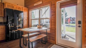 A wooden interior with a black refrigerator, a welcome sign, a table with benches, and a door leading outside. - Sunlit, dog-friendly home with hot tub, gas fireplace, & washer/dryer (Dover)