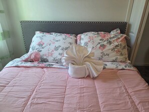 Un lit bien fait, avec une literie à motifs floraux, un coussin décoratif et une serviette pliée.