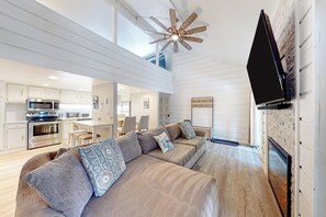 Ein modernes Interieur mit einer Sofagarnitur, einem Flachbildfernseher, einem Deckenventilator und einer Küchenzeile.