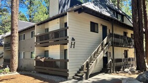 Monikerroksinen rakennus, jossa on parveke toisessa kerroksessa, pääovelle johtavat portaat ja kyltti, jossa on kirjain ’H’, rakennuksen sivulla.
