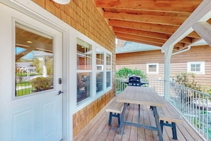 A wooden deck with a table and benches, a barbecue grill, and a white door with windows.