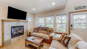 A living room with a fireplace, a large flat-screen TV, a sectional sofa, and a door with a sign reading 'LAKE THIS WAY'.
