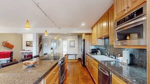 Una cocina moderna con encimeras de granito, armarios de madera, electrodomésticos de acero inoxidable e iluminación colgante.