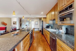 A modern kitchen with granite countertops, wooden cabinets, stainless steel appliances, and pendant lighting. - All-season condo with hot tub, deck, sauna, wood stove & washer/dryer (Mammoth Lakes)