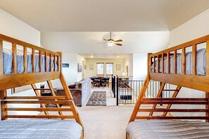 A room with two bunk beds, a ceiling fan, a dining area with a table and chairs, and a staircase leading to an upper level. - Home with patio, grill, fireplace, streaming, washer/dryer & AC (Dover)