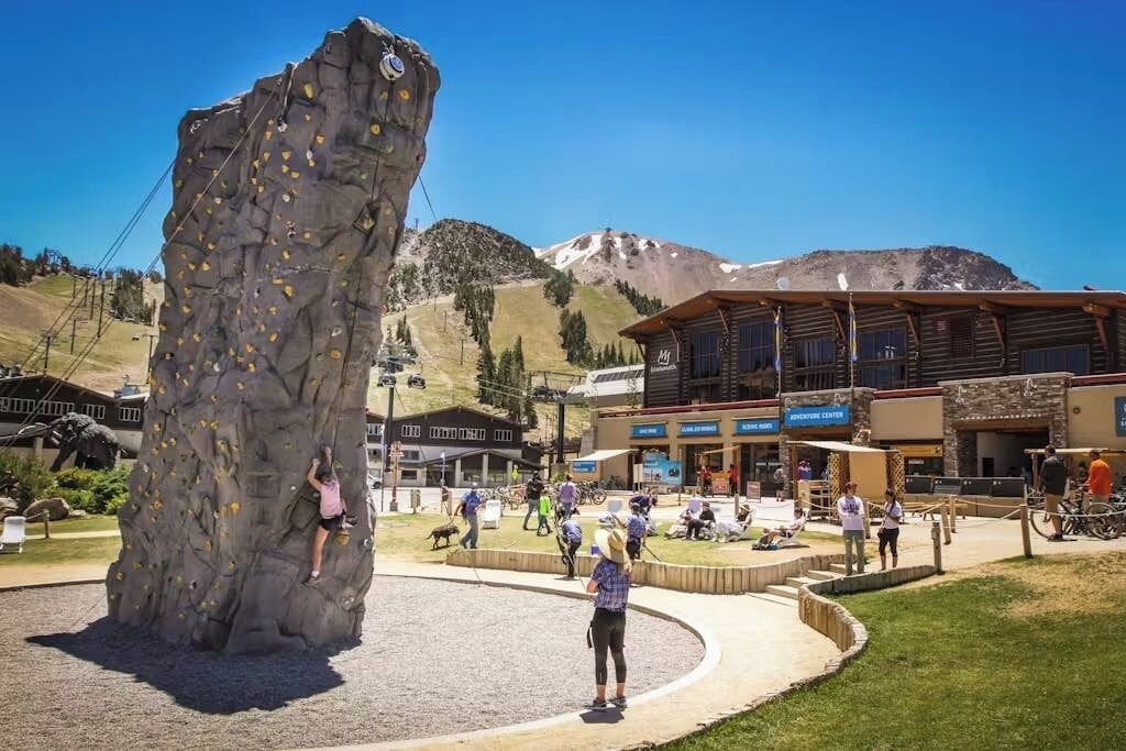 A rock climbing wall, a building with an Adventure Center sign, and a person climbing.
