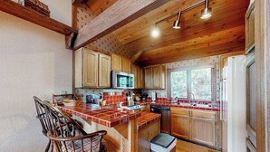 A kitchen with wooden cabinets, a microwave, a sink, and a bar area with chairs. - Mountain view condo with pool, hot tub, sauna & tennis - near ski lifts & golf (Mammoth Lakes)