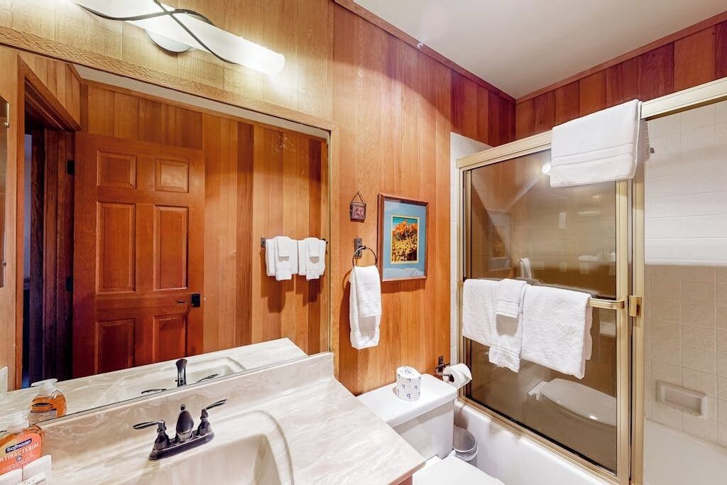 Un baño con pared de paneles de madera, un espejo grande, una ducha con puertas de cristal y un lavabo con encimera de mármol.