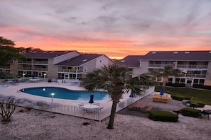 A swimming pool with lounge chairs and a palm tree, surrounded by a building with multiple balconies. - Surfside Retreat, Arcade, Pool, Hot Tub & Tennis (surfside beach)