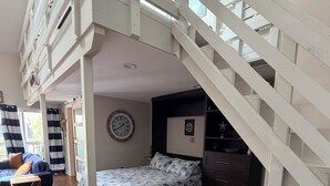Una camera da letto con un letto, una sveglia, un cartello con scritto 'No Wake Time', una scala e un'area pranzo con un tavolo.