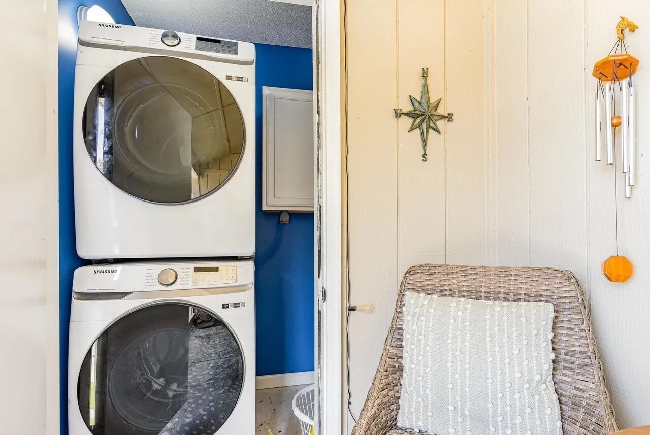 A laundry area with two Samsung washing machines, a white cabinet, and a wicker chair with a white cushion.