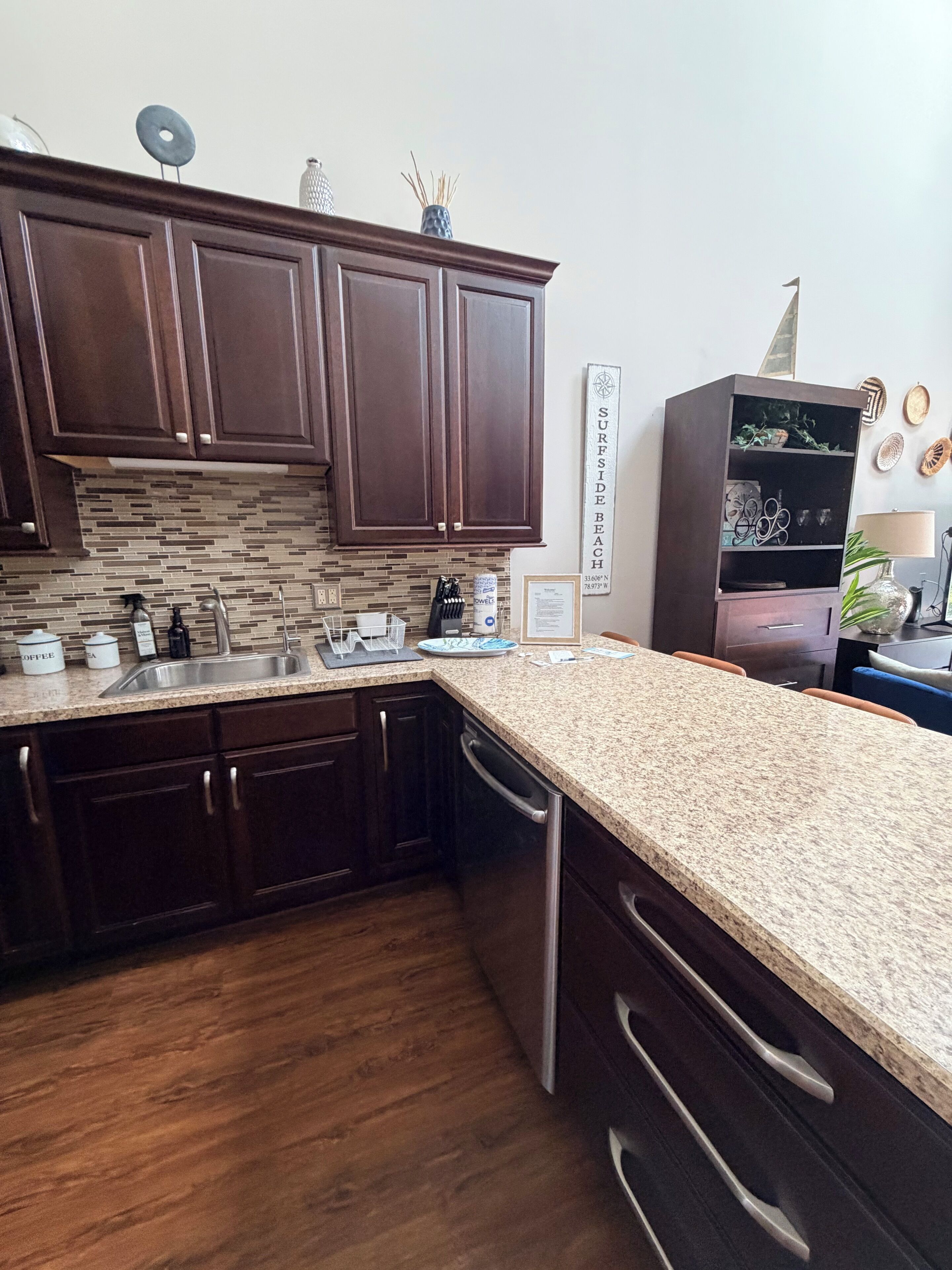 A kitchen with dark wooden cabinets, a granite countertop, a dishwasher, and a decorative wall piece.
