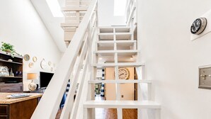 Una scala con ringhiere bianche conduce al secondo piano, con un orologio a parete e una cucina moderna dotata di piano di lavoro e pensili in legno.