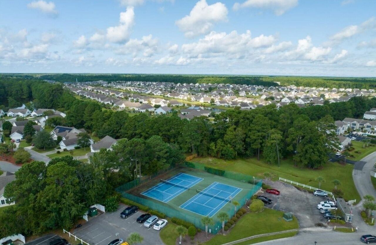 Ett flygbildsbild av ett bostadsområde med en tennisbana omgiven av hus och grönska.