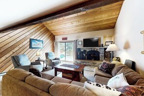 Ein gemütliches Wohnzimmer mit Kamin, Holzbalkendecke und bequemen Sitzmöglichkeiten.