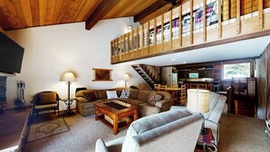 A spacious living area with a high ceiling, a staircase, and a kitchen area. - Lovely mountain-view townhome with hot tub, sauna, & deck views - near skiing (Mammoth Lakes)