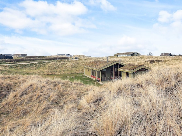 A remote, single-story building with a sloped roof, surrounded by tall grass and dunes. - 6 Person Holiday Home in Lokken (Lokken)