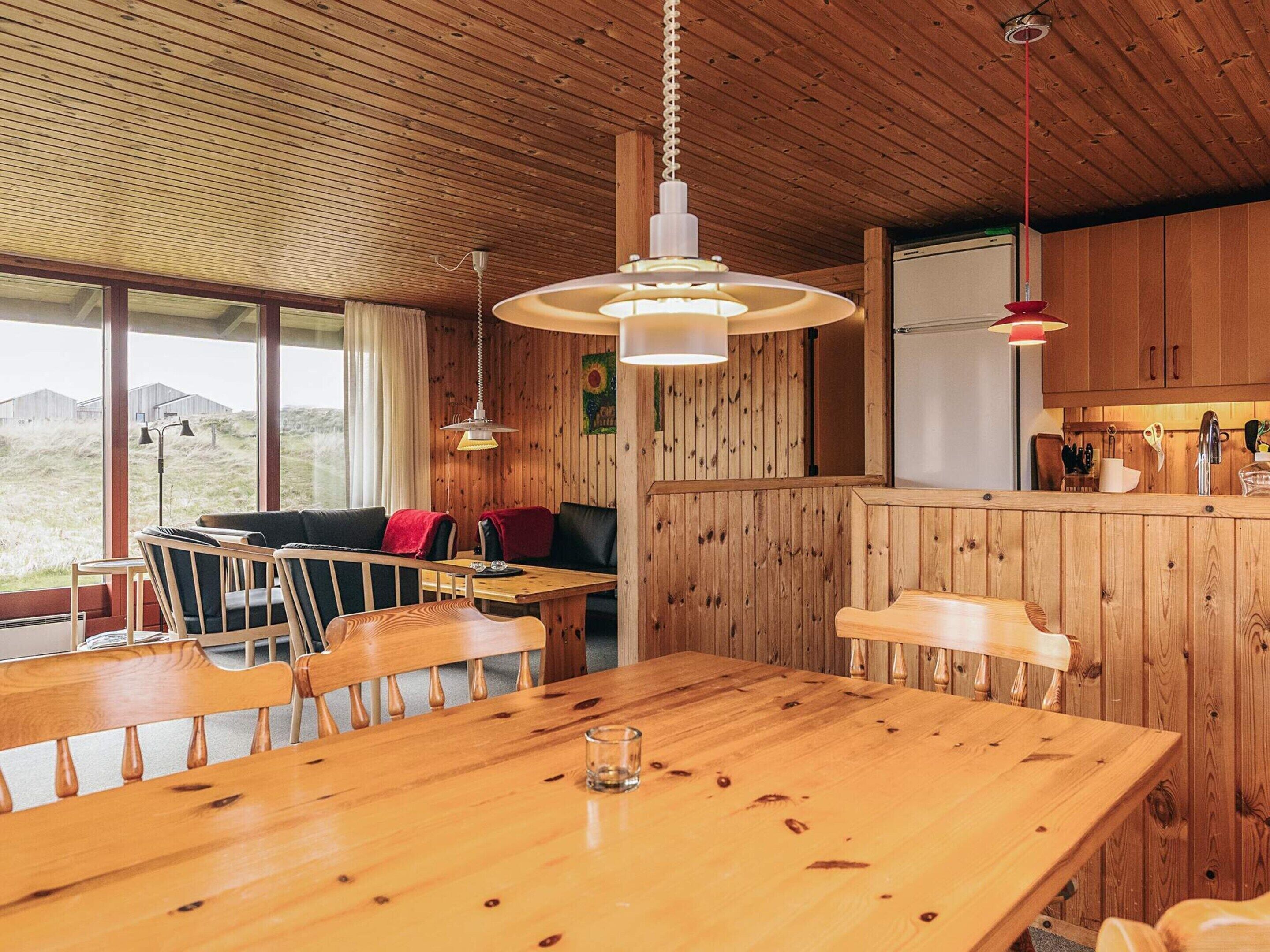 A wooden interior with a dining table, chairs, a sofa, and a kitchen area.