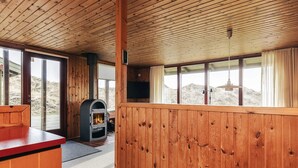 Interior de una cabaña con techo de paneles de madera, chimenea, televisor y ventanas amplias.