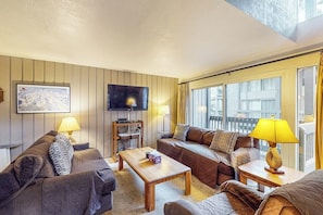 Ein Wohnzimmer mit einer Sofagarnitur, einem Couchtisch, einem Fernseher und einem Fenster mit Vorhängen.