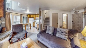 Un salon avec un canapé, un fauteuil et une table basse, un escalier et, au fond, une cuisine.