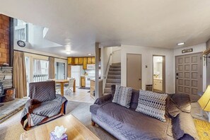 Ein Wohnzimmer mit Sofa, Sessel und Couchtisch, eine Treppe und eine Küche im Hintergrund.