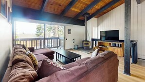 A living room with a wooden ceiling, a sofa, a television, and a fireplace.