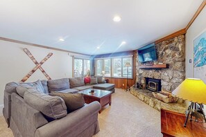 A living room with a sofa, a coffee table, a fireplace, and a television mounted on a stone wall. - Cozy condo w/ shared pool, hot tub & sauna, near outdoor activities (Mammoth Lakes)
