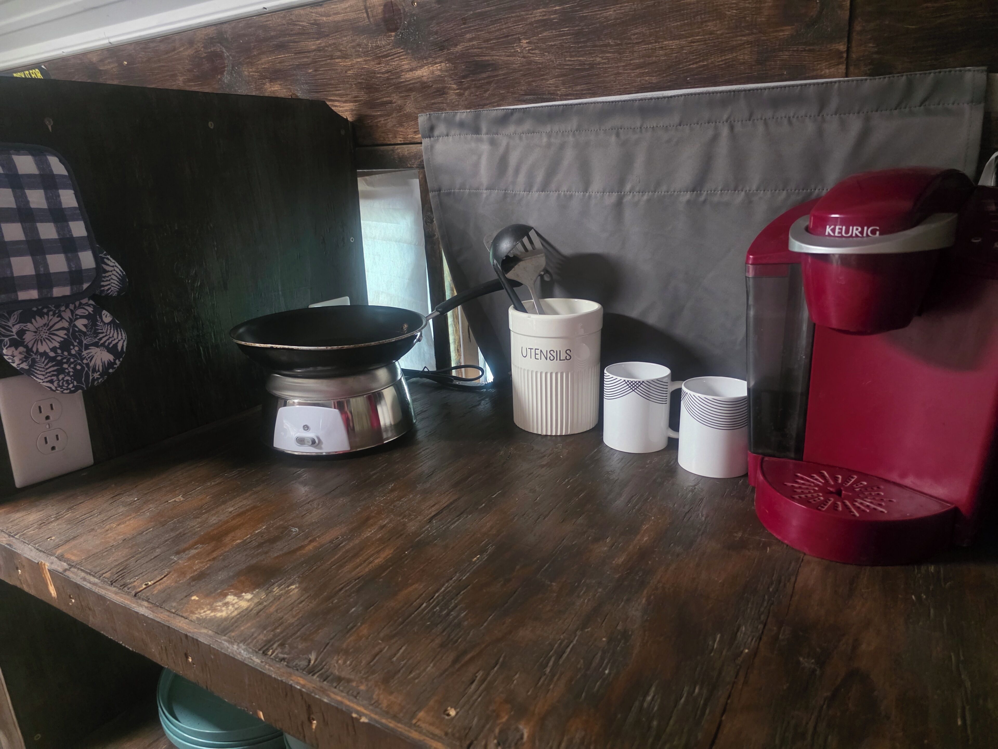 Una encimera de cocina con una estufa portátil, una cafetera Keurig y tres tazas.