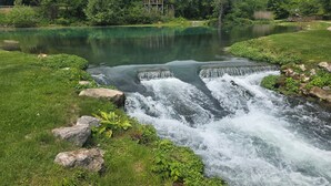 A natural water feature with a small waterfall, surrounded by lush greenery and trees. - Peaceful 1-bedroom caravan with AC in Mammoth Spring. (Mammoth Spring)