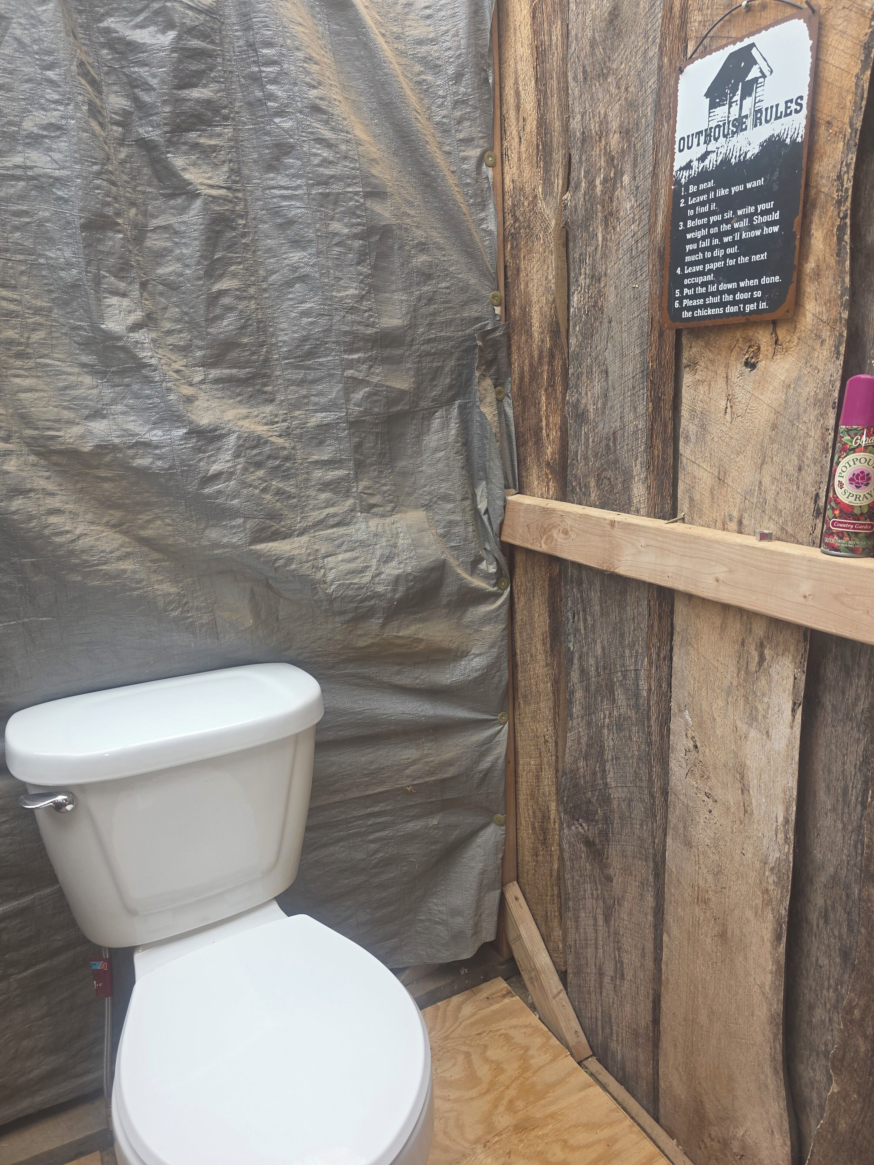 Un letrina rústica con un inodoro blanco, una puerta de madera y un cartel con las normas de uso.