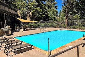 Ein Pool mit Liegestühlen und Grillplatz, umgeben von Bäumen.