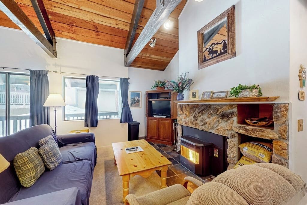 A cozy living room with a stone fireplace, wooden beams, a sofa, a coffee table, and a television.