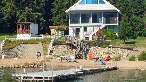 Una casa de dos pisos con un muelle que se adentra en el agua, rodeada de árboles.