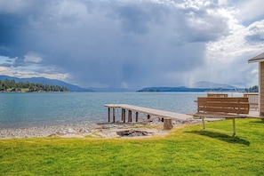 A lakeside view with a wooden dock, a bench, and a building with a deck. - Lakefront home and studio with kayaks, dock, WiFi, fireplaces, BBQ grill (Hope)