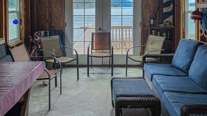 Ein Zimmer mit Seeblick, einer Holzterrasse davor und einem blauen Sofa im Inneren.