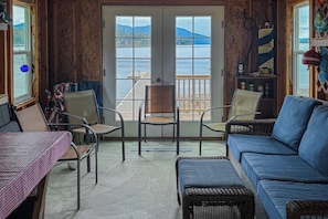 A room with a view of a lake, a wooden deck outside, and a blue sofa inside. - Lakefront home and studio with kayaks, dock, WiFi, fireplaces, BBQ grill (Hope)