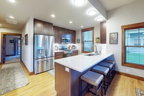 A modern kitchen with stainless steel appliances, a central island with bar stools, and a large window providing natural light. - Elegant, newer, 1st-floor condo with private hot tub - steps to resort marina (Dover)