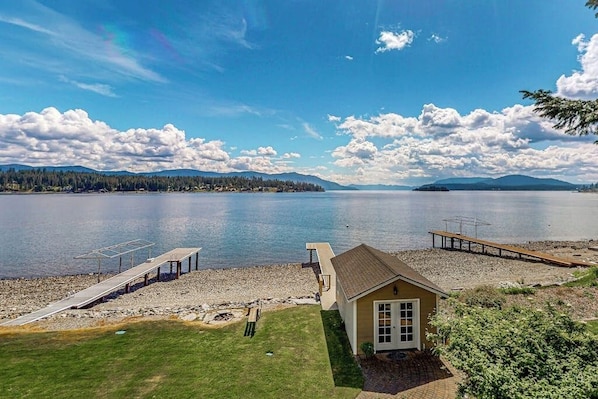 A lakeside property with a dock, a small house, and a grassy area. - Lakefront home with kayaks, dock, WiFi, fireplaces, BBQ grill (Hope)