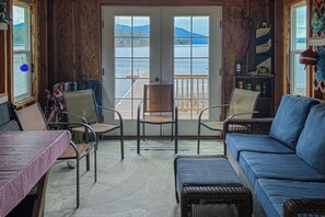 A room with a view of a dock and water, a blue sofa, a dining table, and chairs. - Lakefront home with kayaks, dock, WiFi, fireplaces, BBQ grill (Hope)