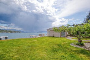 A house with a dock, a grassy yard, and a view of a lake and mountains. - Lakefront home with kayaks, dock, WiFi, fireplaces, BBQ grill (Hope)